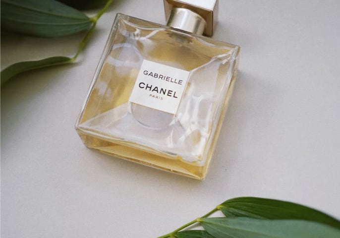 A bottle of Gabrielle Essence laying flat on a white surface, surrounded by leaves